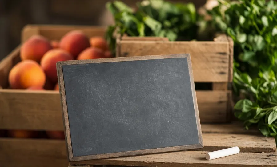 A blank chalkboard propped against wooden crates of peaches.